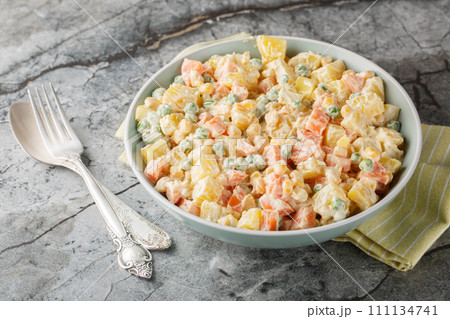 Vegetable salad with potatoes, green peas, carrots, corn and apple covered with mayonnaise close-up on a plate. Horizontal 111134741
