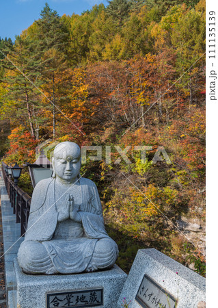 日本　秋田県湯沢市の三途川橋に鎮座している合掌地蔵と紅葉した木々 111135139