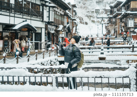 Woman tourist Visiting Ginzan Onsen in Yamagata, happy Traveler sightseeing Japanese Onsen village with Snow in winter season. landmark and popular for attraction in Japan. Travel and Vacation concept Woman tourist Visiting Ginzan Onsen in Yamagata, happy Traveler sightseeing Japanese Onsen village with Snow in winter season. landmark and popular for attraction in Japan. Travel and Vacation concept 111135713