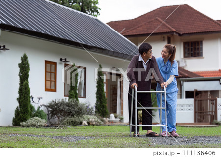 Nurse or caregiver helps elderly walk by using walker in garden 111136406