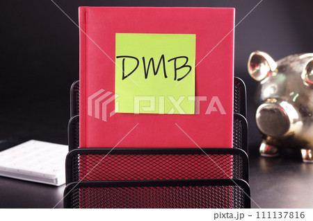 DMB text on a yellow sticker pasted on an upright diary on a black background DMB text on a yellow sticker pasted on an upright diary on a black background 111137816