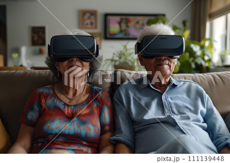 Senior couple at home sitting on couch wearing VR glasses 111139448