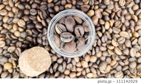 Coffee beans in a small glass jar with a cork lid on the table. Coffee beans packed in a transparent, airtight storage container. Coffee seeds inside a glass jar. Flat layout Coffee beans in a small glass jar with a cork lid on the table. Coffee beans packed in a transparent, airtight storage container. Coffee seeds inside a glass jar. Flat layout 111142029