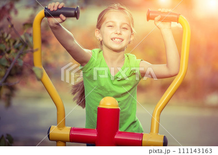 Little girl does exercises at simulator in park Little girl does exercises at simulator in park 111143163