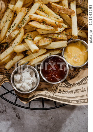 French fries with ketchup and mayonnaise in a basket on a gray background French fries with ketchup and mayonnaise in a basket on a gray background 111143295