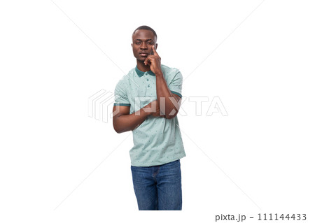 young smart african man dressed in t-shirt and jeans stands holding his chin and thinks young smart african man dressed in t-shirt and jeans stands holding his chin and thinks 111144433