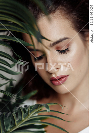 Beautiful woman with perfect skin and natural make-up holding tropical leaves Beautiful woman with perfect skin and natural make-up holding tropical leaves 111144924