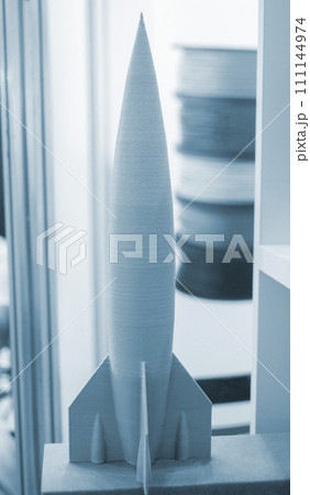 Art object model rocket printed on 3D printer. Rocket toy created by 3D printing from molten plastic. Example creating prototype by 3D printer. Concept 3D printing. 3D printing innovation technology 111144974