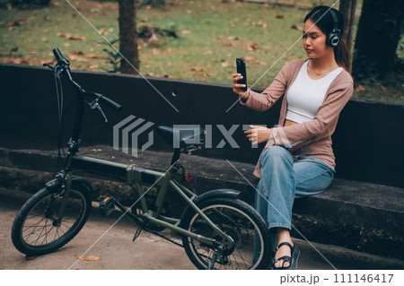 Happy young Asian woman while riding a bicycle in a city park. She smiled using the bicycle of transportation. Environmentally friendly concept. Happy young Asian woman while riding a bicycle in a city park. She smiled using the bicycle of transportation. Environmentally friendly concept. 111146417