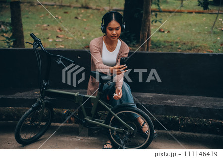 Happy young Asian woman while riding a bicycle in a city park. She smiled using the bicycle of transportation. Environmentally friendly concept. Happy young Asian woman while riding a bicycle in a city park. She smiled using the bicycle of transportation. Environmentally friendly concept. 111146419