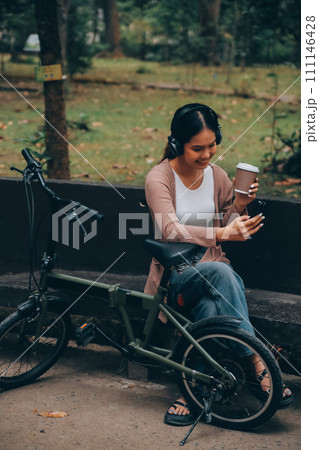 Happy young Asian woman while riding a bicycle in a city park. She smiled using the bicycle of transportation. Environmentally friendly concept. Happy young Asian woman while riding a bicycle in a city park. She smiled using the bicycle of transportation. Environmentally friendly concept. 111146428
