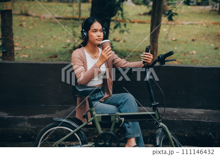Happy young Asian woman while riding a bicycle in a city park. She smiled using the bicycle of transportation. Environmentally friendly concept. Happy young Asian woman while riding a bicycle in a city park. She smiled using the bicycle of transportation. Environmentally friendly concept. 111146432