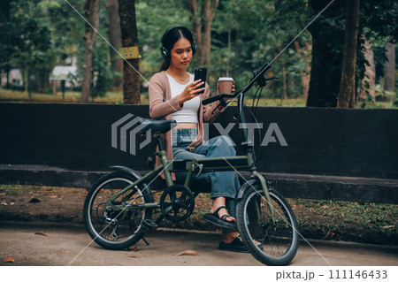 Happy young Asian woman while riding a bicycle in a city park. She smiled using the bicycle of transportation. Environmentally friendly concept. Happy young Asian woman while riding a bicycle in a city park. She smiled using the bicycle of transportation. Environmentally friendly concept. 111146433