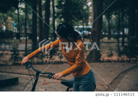 Happy young Asian woman while riding a bicycle in a city park. She smiled using the bicycle of transportation. Environmentally friendly concept. 111146515