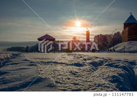 A snow-covered beach with protruding beach umbrellas under a blue sky and a bright sun at sunset A snow-covered beach with protruding beach umbrellas under a blue sky and a bright sun at sunset 111147783
