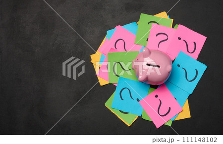 Ceramic piggy bank and stickers with drawn question marks on a black background, top view 111148102