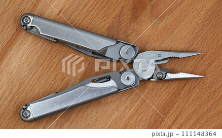 One modern open folding multifunctional knife made of gray iron on a wooden background. Multitool with extended tools and pliers. Compact and portable product. Pocket knife. EDC concept 111148364