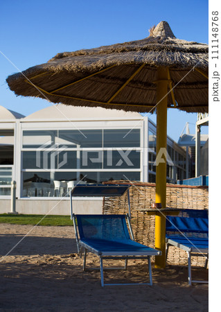 Sun lounger under a straw umbrella on a sandy beach for relaxing in the shade from the sun on a hot day in Egypt Sun lounger under a straw umbrella on a sandy beach for relaxing in the shade from the sun on a hot day in Egypt 111148768