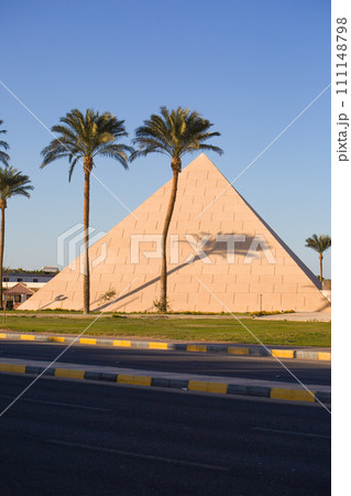 Building in the shape of an Egyptian pyramid with palm trees near the road. Like a great landmark 111148798