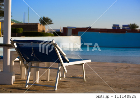 Sun lounger under a sun umbrella near the pool in a hotel, a place to relax outdoors on vacation Sun lounger under a sun umbrella near the pool in a hotel, a place to relax outdoors on vacation 111148828
