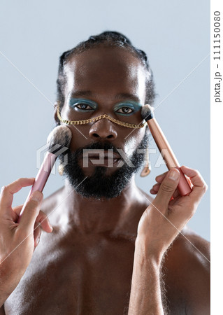 Bearded gay man applying makeup with brushes held Bearded gay man applying makeup with brushes held 111150080