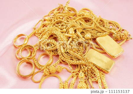 Many gold necklaces and gold bars on pink fabric background. Many gold necklaces and gold bars on pink fabric background. 111153137