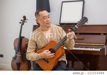 Happy asian man senior elderly take it easy on retirement holidays playing guitar Happy asian man senior elderly take it easy on retirement holidays playing guitar 111153364