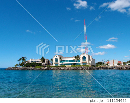Buildings side at waters edge protected by a lava rock sea wall with a radio tower towering above Buildings side at waters edge protected by a lava rock sea wall with a radio tower towering above 111154453