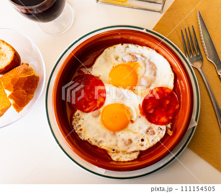 Popular dish of spanish cuisine, fried eggs with chorizo sausages and tomato paste served on plate 111154505