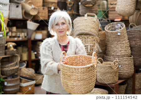 Senior woman looks at wicker basket in store. 111154542