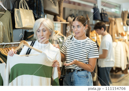 Young girl consults senior female friend about purchasing sweater during shopping 111154706