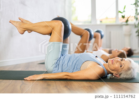 Family grandmother, mother and granddaughter perform fitness exercises lying on floor with softball. 111154762