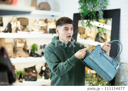 Guy customer is amazed to read price tag on leather handbag in store Guy customer is amazed to read price tag on leather handbag in store 111154877
