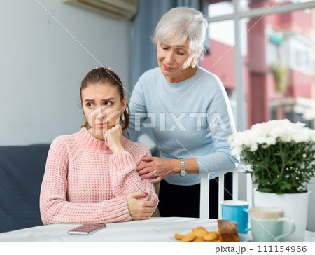 Careful elderly mother comforting upset adult daughter at table Careful elderly mother comforting upset adult daughter at table 111154966