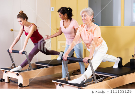 Two active women perform an exercise using a reformer bed Two active women perform an exercise using a reformer bed 111155129