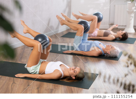 Fitness family in activewear working out with soft ball pilates on mat while doing upper body training in yoga studio Fitness family in activewear working out with soft ball pilates on mat while doing upper body training in yoga studio 111155254