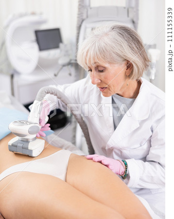 Old woman specialist doing LPG massage of belly of young woman Old woman specialist doing LPG massage of belly of young woman 111155339