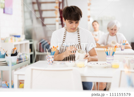 Skilled young artist painting ceramic cup in pottery workshop 111155579