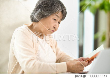 年金手帳を見ながらパソコンを使うシニア女性 終活 年金手帳を見ながらパソコンを使うシニア女性 終活 111158834