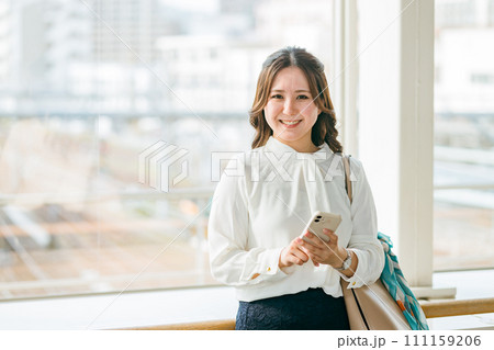 駅のロビーでスマホを使う笑顔の女性（アプリ・モバイルチケット・チケットレス・電子乗車券） 111159206