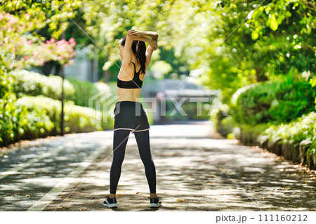 緑の中でストレッチをするスポーツウエアの若い女性 111160212