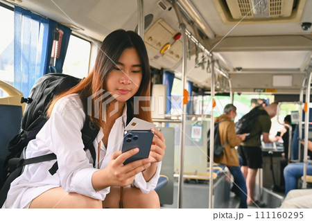Happy Asian female tourist holding credit card and using smartphone while commuting by bus 111160295