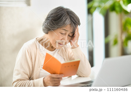 年金手帳を見ながらパソコンを使うシニア女性　終活 111160486
