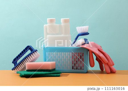 A blue basket with detergents, pink gloves, sponges and brushes on pastel blue background. Front view, minimal scene for advertising with copy space. Cleaning service concept A blue basket with detergents, pink gloves, sponges and brushes on pastel blue background. Front view, minimal scene for advertising with copy space. Cleaning service concept 111163016