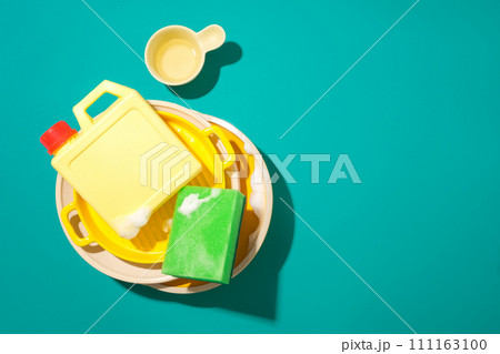 A bottle of detergent and a sponge are placed on top of a pile of dirty dishes on a turquoise background. Free space for text design and product display. 111163100
