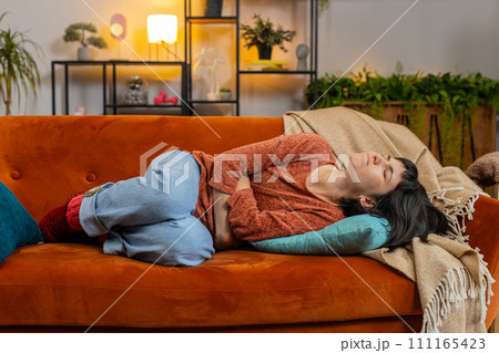 Upset woman embracing belly suffering from stomachache, menstrual painful feelings lying on sofa Upset woman embracing belly suffering from stomachache, menstrual painful feelings lying on sofa 111165423