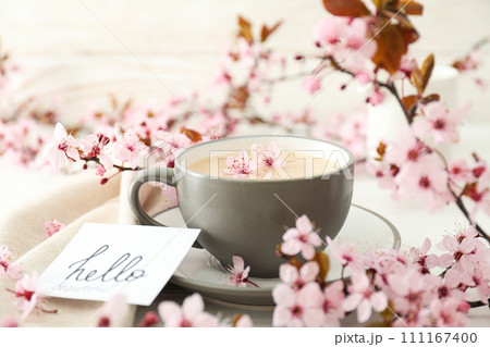 Spring twigs with flowers with a cup of hot drink, on a light wooden background. 111167400