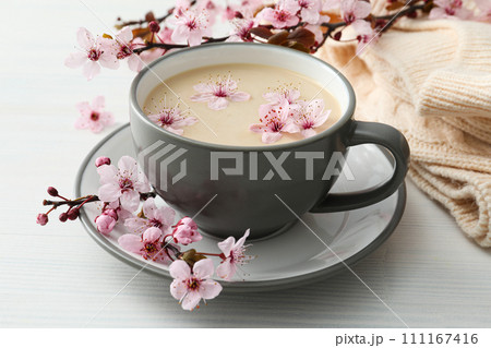 Spring twigs with flowers with a cup of hot drink, on a light wooden background. 111167416