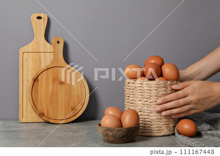 Eggs in a wicker basket, with a hand, on a gray background. 111167448
