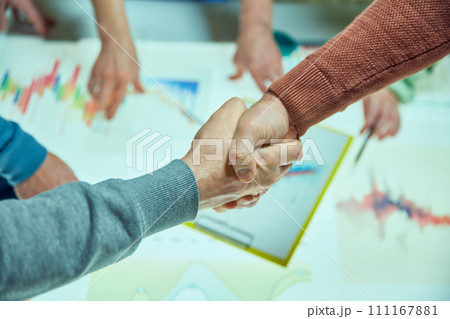 Two people shaking hands over a table with business graphs, symbolizing agreement and partnership. Start of new project and cooperation Two people shaking hands over a table with business graphs, symbolizing agreement and partnership. Start of new project and cooperation 111167881